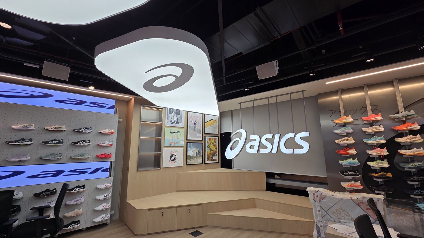 Loja ASICS com iluminação Blinkie: luminária suspensa com logo retroiluminado, painéis de calçados e letreiro iluminado